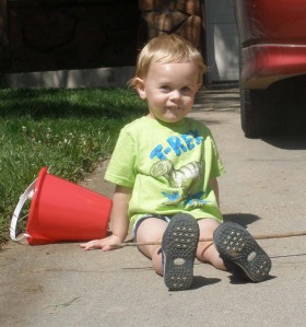 small boy sits in driveway with bucket 